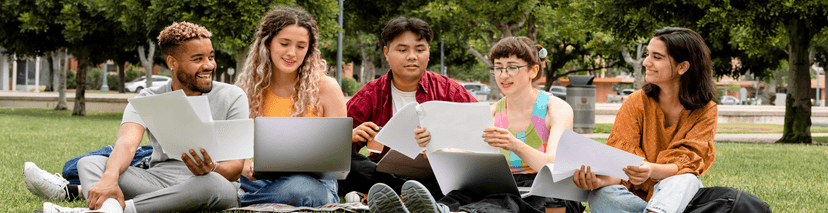 Group of 5 students sitting in the grass comparing notes