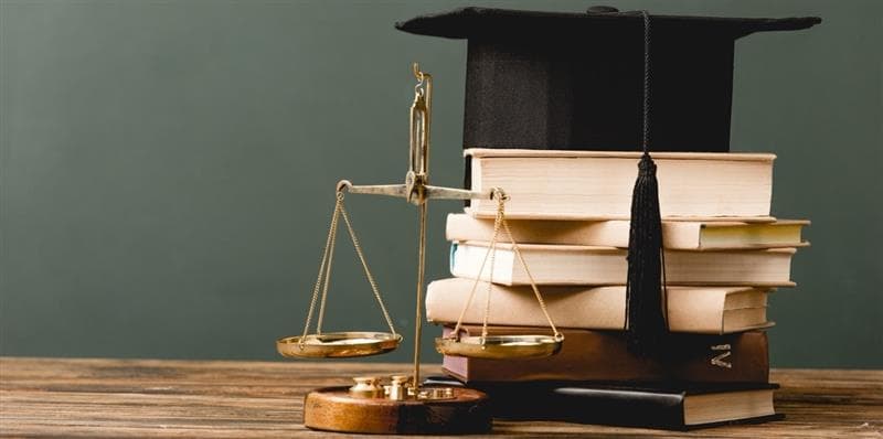 A scale and a pile of books with a graduation cap on top.