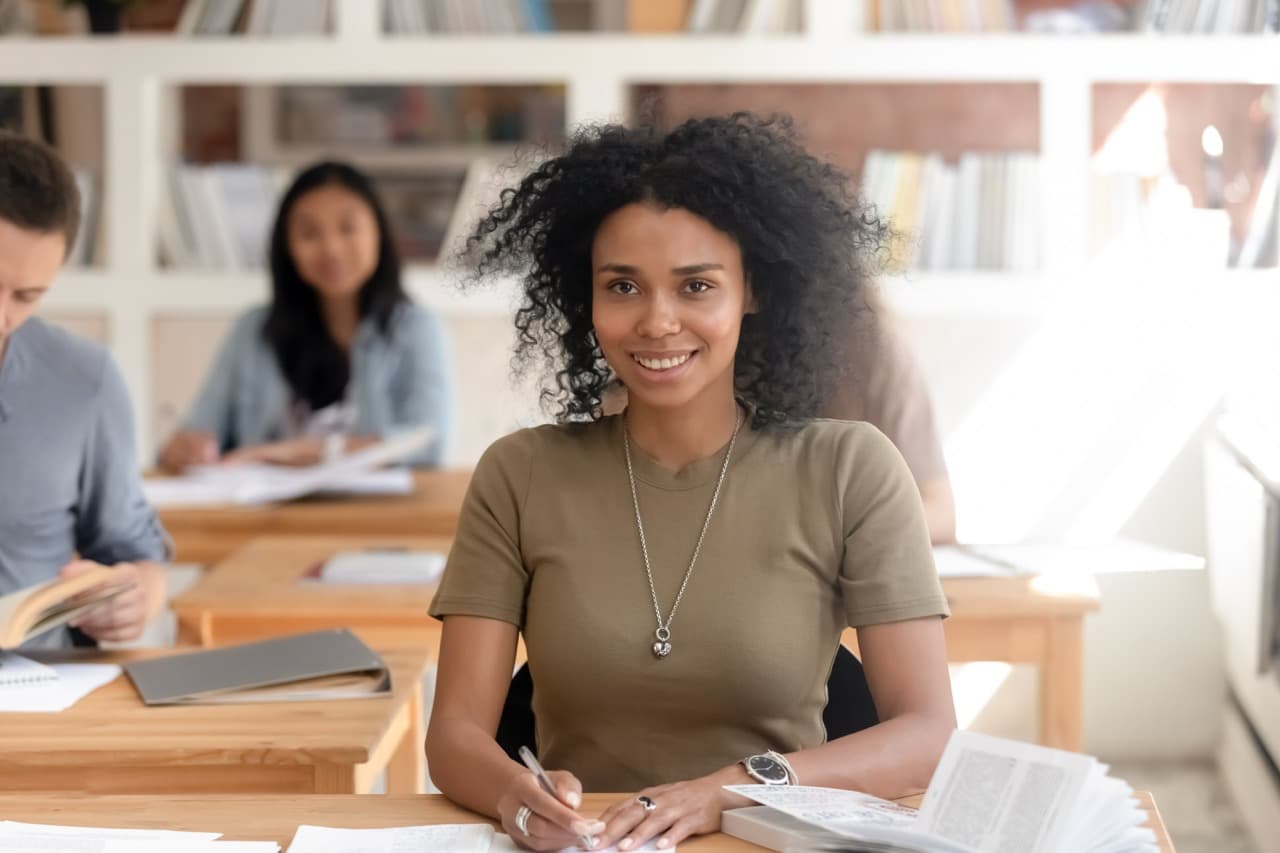 A student in focus sitting in a classroom with three other students in the same setting.