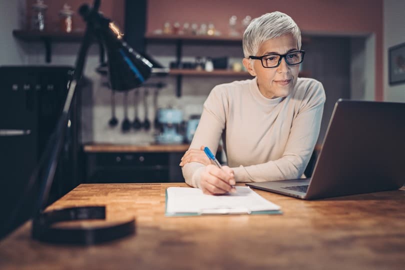 Woman Writing While Looking at Laptop