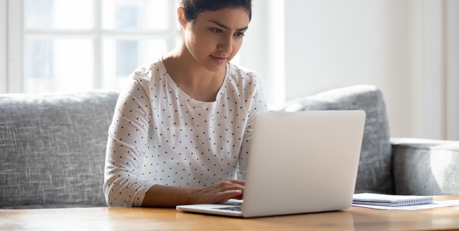 A woman sitting on a couch, focused on her laptop screen.